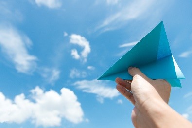 photo d'une main tenant un avion en papier avec le ciel en fond