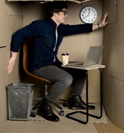 photo
salarié sur sa chaise devant un petit bureau avec son ordinateur, son café, sa poubelle et son horloge dans une petit espace en carton